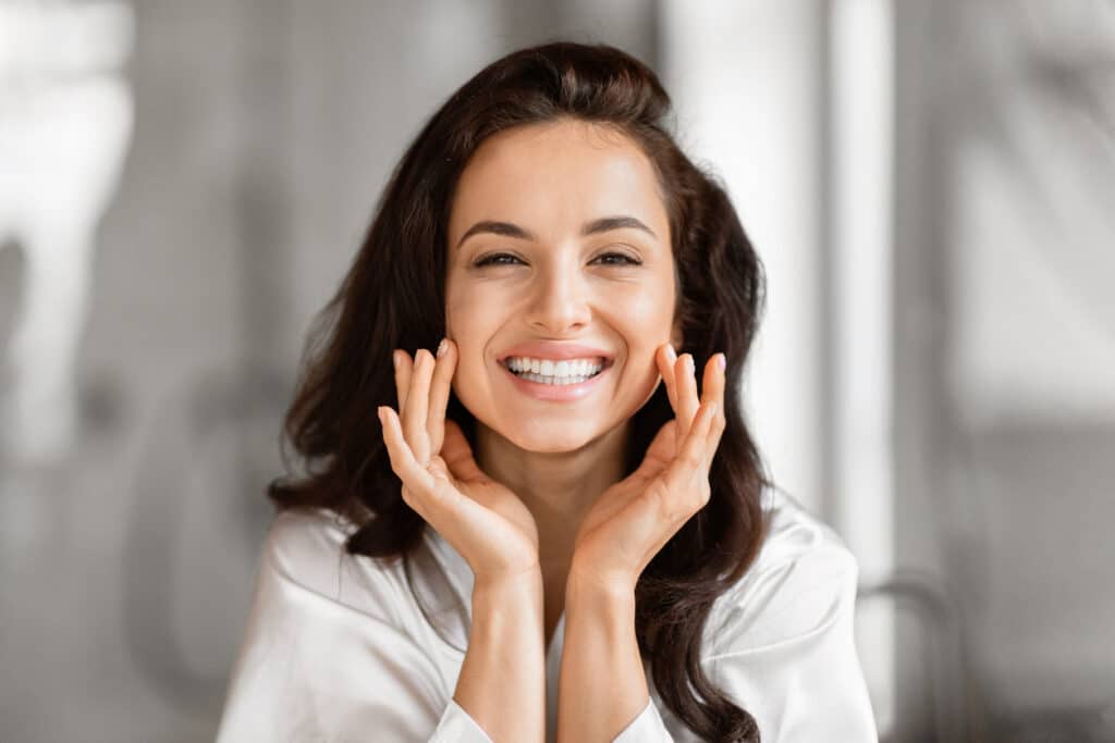 Smiling woman touching her cheeks, showing smoother-looking skin resulting from a chemical peel treatment.